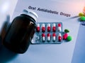 Diabetes drugs in packs and and medicine bottle with blank label placed on textbook. Green tablets and pink-white capsule pills.