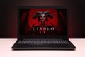 Diablo 4 game on the screen laptop computer on black textured wall with red light.