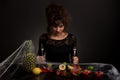 The diabolical young girl sitting at a table with fruits covered with spider web