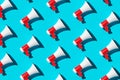 Diagonal array pattern of white and red megaphones or bullhorns over cyan blue background, business announcement or communication