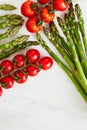 Diagonal composition of asparagus stems and branches of cherry tomatoes on a off-white rustic table.