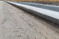 Diagonal view of fresh extruded curbing on a road construction site, dirt street bed