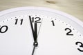 Dial of an analog clock close up on a wooden background. The time is 23:59. White dial, black numerals