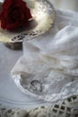 A diamond engagement ring sitting on a lace scarf on an ornate vintage metal stand with a silver tray holding a single red rose Royalty Free Stock Photo