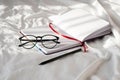 Diary, pencil and eyeglasses rest on white bedding in sunlight with shadows.  Personal journal for notes. Royalty Free Stock Photo