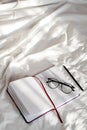 Diary, pencil and eyeglasses rest on white bedding in sunlight with shadows.  Personal journal for notes. Royalty Free Stock Photo