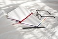 Diary, pencil and eyeglasses rest on white bedding in sunlight with shadows. Personal journal for notes.