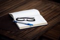 Diary on a wooden table. Glasses and pen