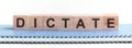 DICTATE - a word made of wooden blocks with black letters, a row of blocks is located on a blue Notepad