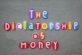 The dictatorship of money, social slogan composed with multi colored stone letters over green sand
