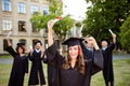 We did it! Happy grad girl is smiling, group of her friends class mates are behind. She is in a black mortar board, with red tass Royalty Free Stock Photo