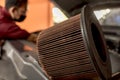 An diesel air filter lies on the hood of a SUV while a mechanic at the back does routine maintenance