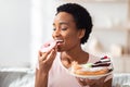 Diet breakdown, cheat meal and imbalanced nutrition. Young black woman with plate of sweets eating donut at home