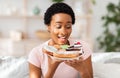 Diet breakdown and unhealthy nutrition concept. Young African American lady holding plate of sweet pastries at home