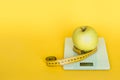 Diet concept. Apples and table top kitchen scales and measuring tape line on yellow background.