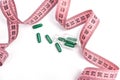 Diet concept. Diet pills, green capsules with pink measuring tape on a white background