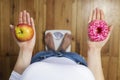 Diet concept. Dieting young woman measuring body weighing on weight scale, hold sweet donut and red apple, making choice between Royalty Free Stock Photo