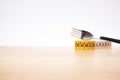 Diet concept - fork with spiraled measure tape on a wooden table surface