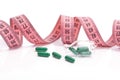 Diet concept. Diet pills, green capsules with pink measuring tape on a white background