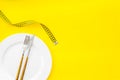 Diet concept with plate, flatware and measuring tape for weight loss on yellow background top view mock up