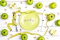 Diet concept table setting with cutlery, yellow measuring tape and green apples on white wooden table.