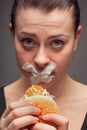 Diet concept: woman holding a burger with mouth sealed