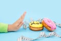 Diet or good health concept. hand rejecting unhealthy food like donuts or dessert isolated on blue background
