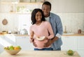 Diet for healthy pregnancy. Positive black guy hugging his lovely expectant wife with balanced meal in kitchen Royalty Free Stock Photo