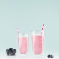 Diet milk beverages in elegant glass with blueberries in bowl, striped straws on pastel soft light blue background, square.