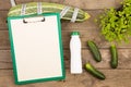 marrow squash, measure tape, blank clipboard, bottle of water and cucumbers on brown wooden table Royalty Free Stock Photo