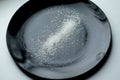 Diet: several spoonfuls of sugar beet crystal scattered over a dark plate on a white background