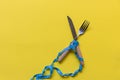 Diet slimming. Blue Measuring tape wrapped around wood fork lying on yellow background.
