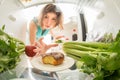 Diet struggle: A hand grabbing a donut from the open refrigerator full of greens. Royalty Free Stock Photo