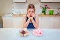 Diet struggle. Young sad woman in blue T-shirt chooses between fresh fruit vegetables or sweets while looking at them in