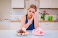 Diet struggle. Young sad woman in blue T-shirt chooses between fresh fruit vegetables or sweets while looking at them in Royalty Free Stock Photo