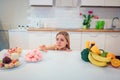 Diet struggle. Young sad woman in blue T-shirt choosing between fresh fruit vegetables or sweets in the kitchen. Choice Royalty Free Stock Photo