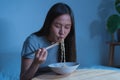 Diet, templtation. Alone asian young student woman, girl using chopsticks eating instant ramen, noodles in bowl on table in Royalty Free Stock Photo