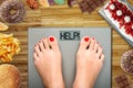 Diet temptation or hard to lose weight concept with woman weighing on bathroom scale with many sweets and fast food around