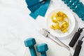 Diet, weight loss concept. Flat lay plate with centimetre tape, cutlery, dumbbells, scales and fitness equipment on white marble