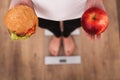 Diet. Woman Measuring Body Weight On Weighing Scale Holding Burger and apple. Sweets Are Unhealthy Junk Food. Dieting, Healthy Eat Royalty Free Stock Photo