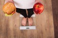 Diet. Woman Measuring Body Weight On Weighing Scale Holding Burger and apple. Sweets Are Unhealthy Junk Food. Dieting, Healthy Eat Royalty Free Stock Photo