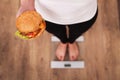 Diet. Woman Measuring Body Weight On Weighing Scale Holding Burger and apple. Sweets Are Unhealthy Junk Food. Dieting, Healthy Eat Royalty Free Stock Photo