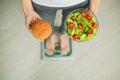 Diet. Woman Measuring Body Weight On Weighing Scale Holding Burger and Salad. Sweets Are Unhealthy Junk Food. Dieting Royalty Free Stock Photo