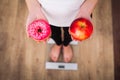 Diet. Woman Measuring Body Weight On Weighing Scale Holding Donut and apple. Sweets Are Unhealthy Junk Food. Dieting, Healthy Eat Royalty Free Stock Photo