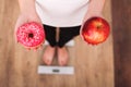 Diet. Woman Measuring Body Weight On Weighing Scale Holding Donut and apple. Sweets Are Unhealthy Junk Food. Dieting, Healthy Eati Royalty Free Stock Photo
