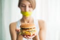 Diet. Young woman with duct tape over her mouth, preventing her to eat junk food. Healthy eating concept Royalty Free Stock Photo