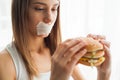 Diet. Young woman with duct tape over her mouth, preventing her to eat junk food. Healthy eating concept Royalty Free Stock Photo