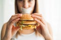 Diet. Young woman with duct tape over her mouth, preventing her to eat junk food. Healthy eating concept Royalty Free Stock Photo