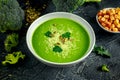 Dietary Broccoli smooth cream soup with sprinkle of sunflower seeds, parsley leaves and croutons on stone table.