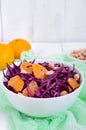 Dietary spicy salad of red cabbage, tangerine and raw peanuts in a ceramic bowl on a white wooden background.